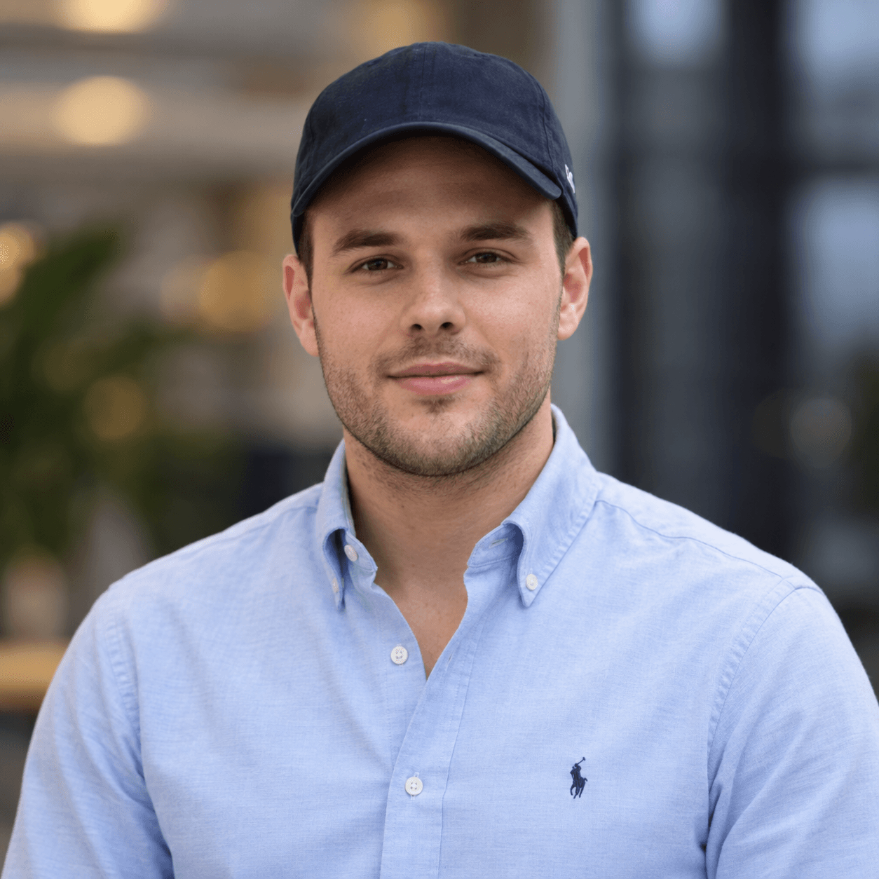 A young man, casually dressed in a blue baseball cap and polo shirt, offers a confident look to the camera.