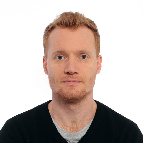 A professional headshot features a man with reddish hair and a beard, looking directly at the camera.