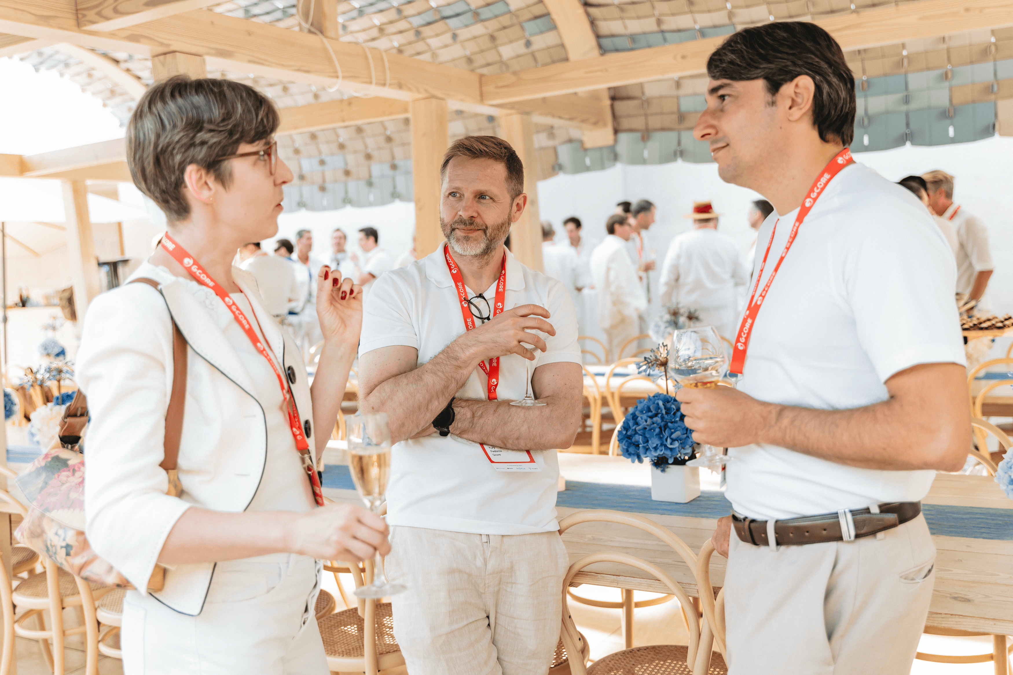 Three people in light clothing engaged in conversation at a sunny outdoor event.